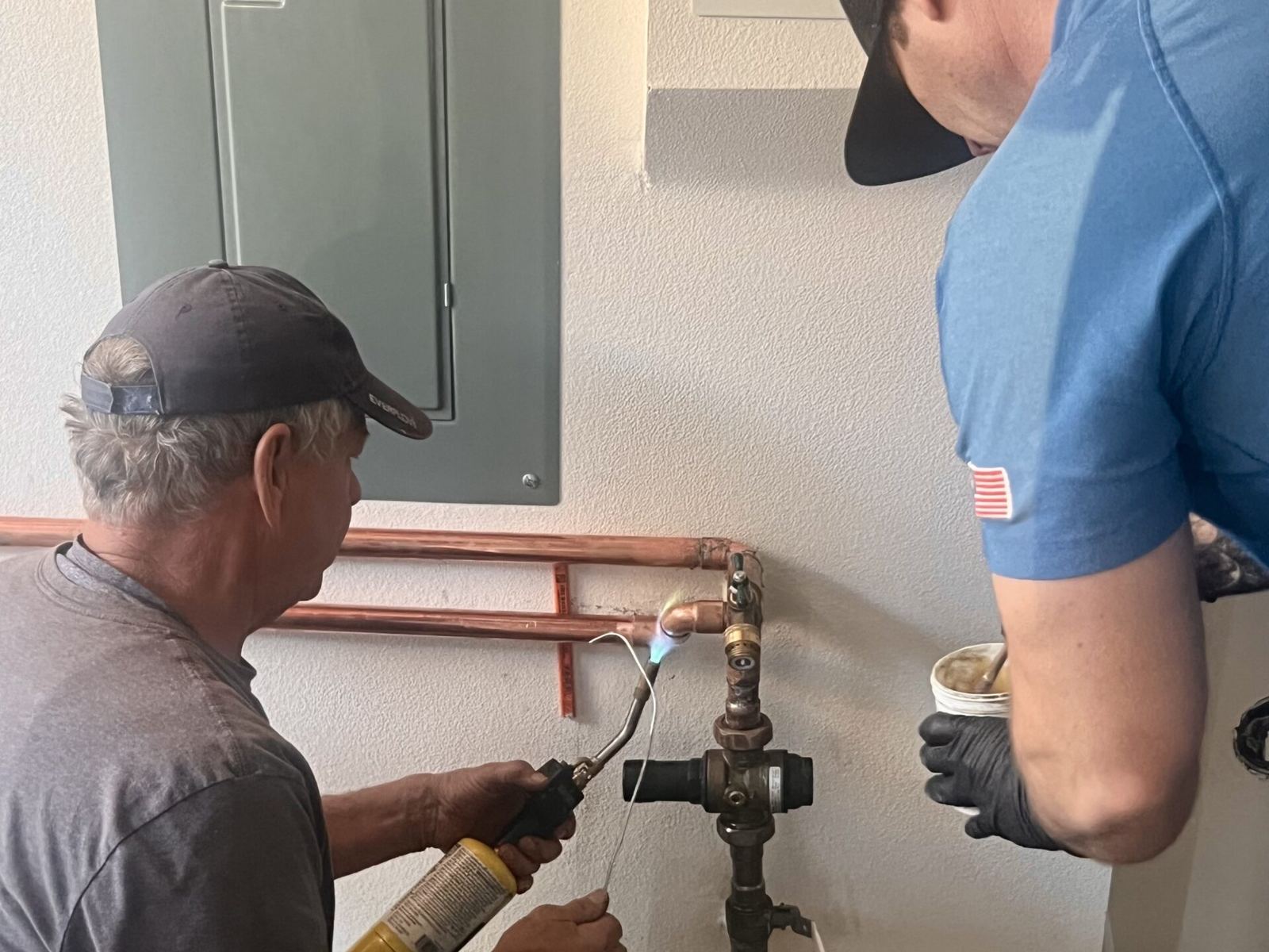 Two Nuvia employees soldering a copper connection at a home's main water line