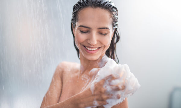 Portrait of happy girl taking shower with gel. She washing with puff