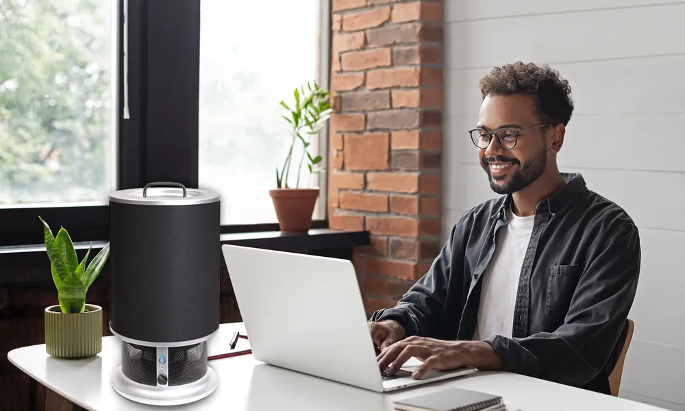 A man working on a laptop at a desk beside a Nuvia Breeze air purifier