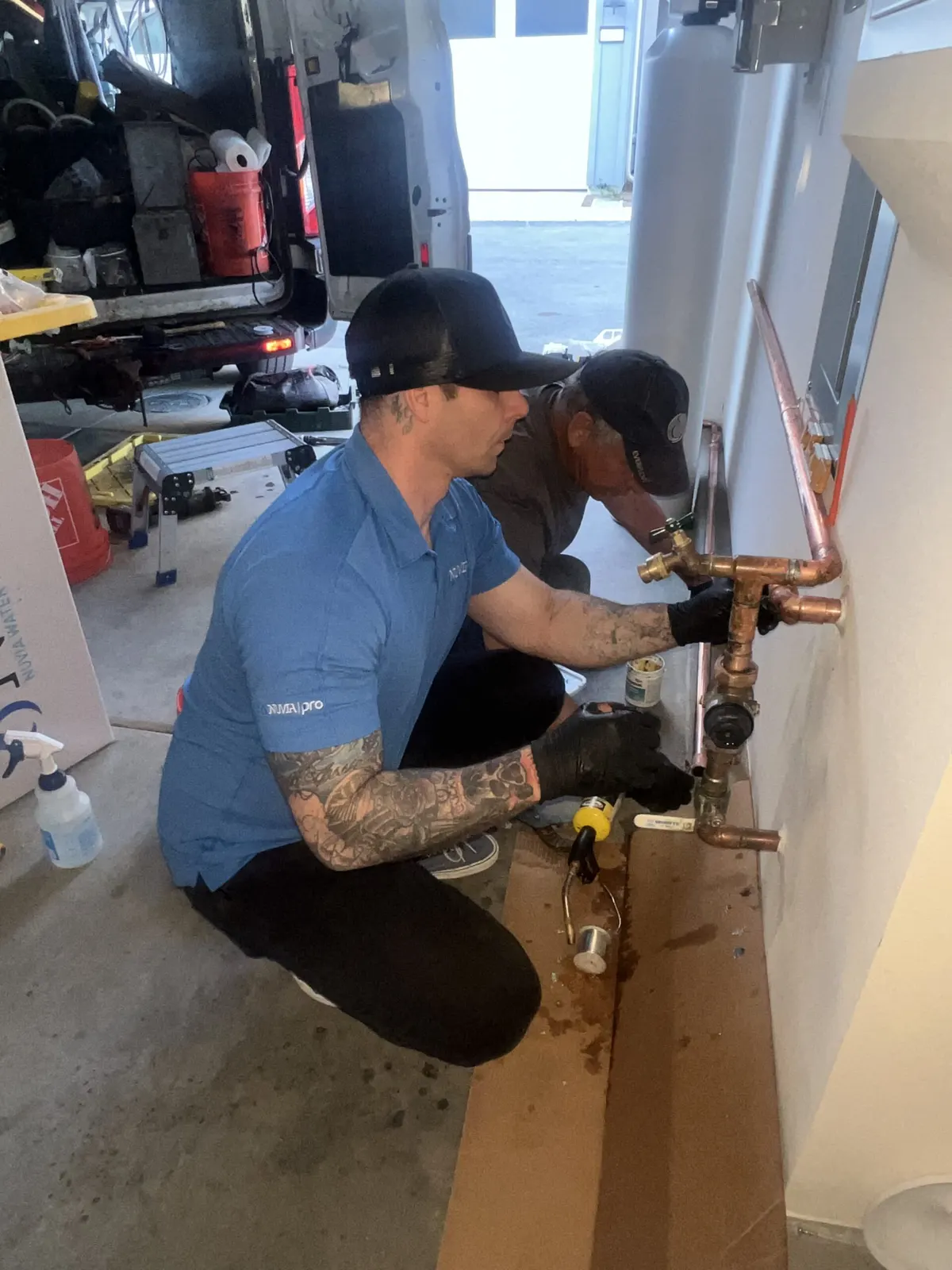 Two Nuvia installers soldering a copper water loop on a garage wall