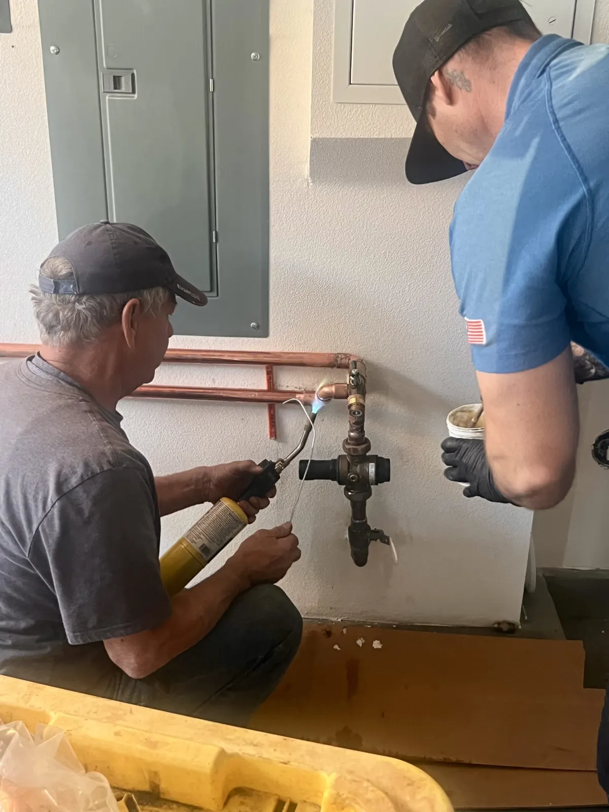 Two Nuvia installers working on a copper water line at a garage wall