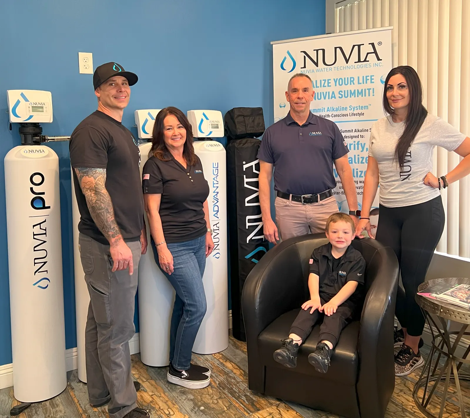Four adults and a child in Nuvia shirts beside Nuvia Pro and Nuvia Advantage systems and a Nuvia banner