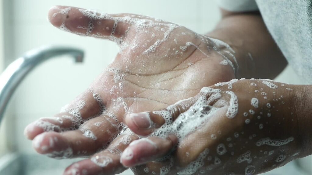 Person showering with visible hard water mineral buildup on bathroom glass.